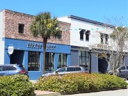 Blue and Red Brick Building with Silver Bluff Brewing Co sign next to White & Gray Building Palm tree and plants in foreground
