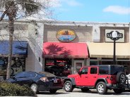 Tan Brick Building With Multiple Businesses. Blue, Red and Beige Awnings. Red Jeep Center Building Sign says Nautica Joe's